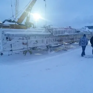 Подготовка буровой установки к погрузке краном на заснеженной промышленной площадке