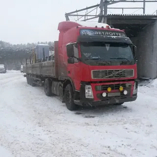 Грузовой автомобиль Volvo с бортовым полуприцепом на заснеженной промышленной площадке